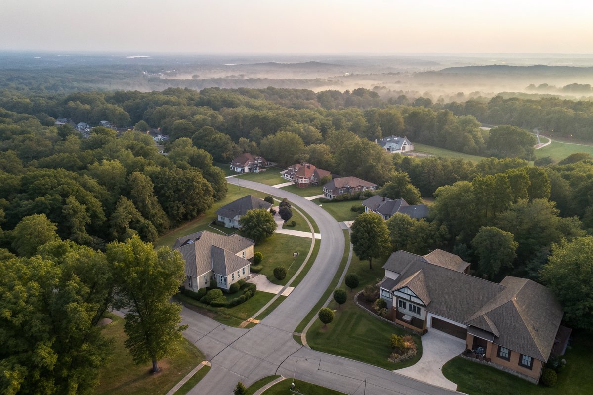 Aerial view of a suburban subdivision with gray and brown shingle roofs along curving streets through mature oaks
